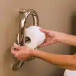 A woman changing a toilet paper roll on an Invisia wall toilet paper roll holder.