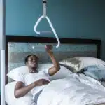 A woman using a SuperPole with a SuperTrapeze to pull herself to a sitting position while laying down in bed.