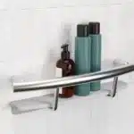 The Invisia Shampoo Shelf and grab bar installed on white tile holding several shampoo bottles.