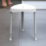 3-legged, white shower stool on a tile floor
