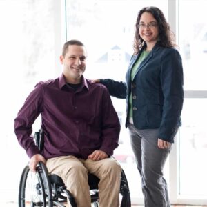 Photo of a woman standing next to a man in a wheelchair; Sarah and Scott Pruett, co-founders of The Universal Design Project.