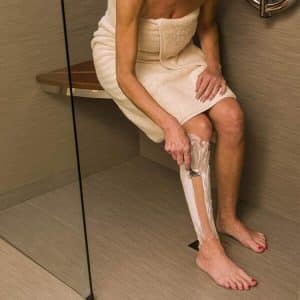 Woman sitting on the Invisia Corner Seat and she is shaving her legs